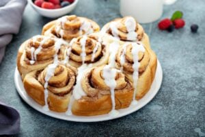 Round platter of gooey cinnamon rolls with cream cheese icing on distressed counter